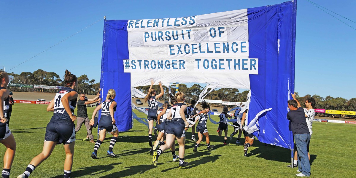 Women's Sports Team Running on Sports Field Beneath Flag