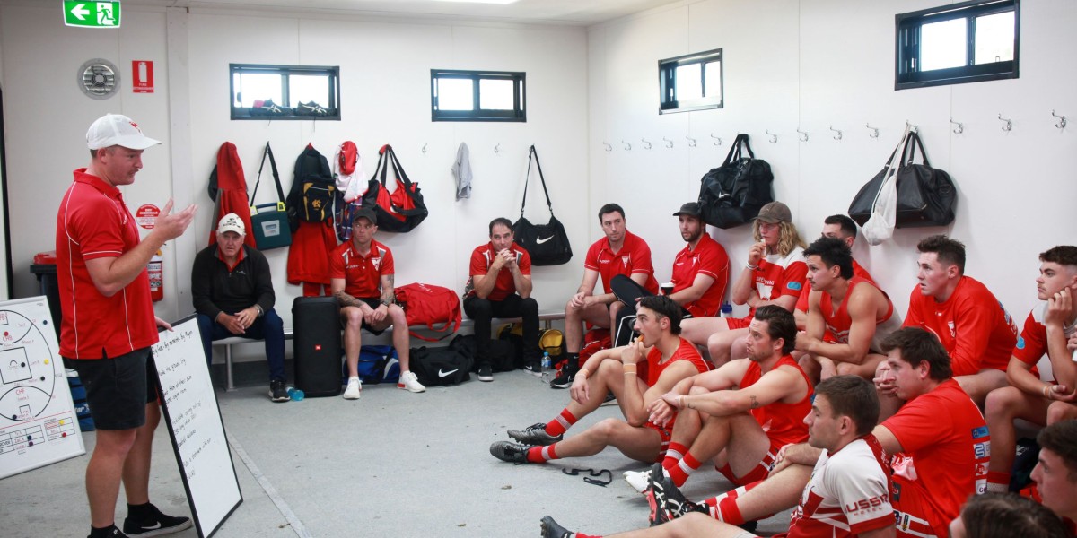 Male Sports Team Sitting in Changeroom with a Coach