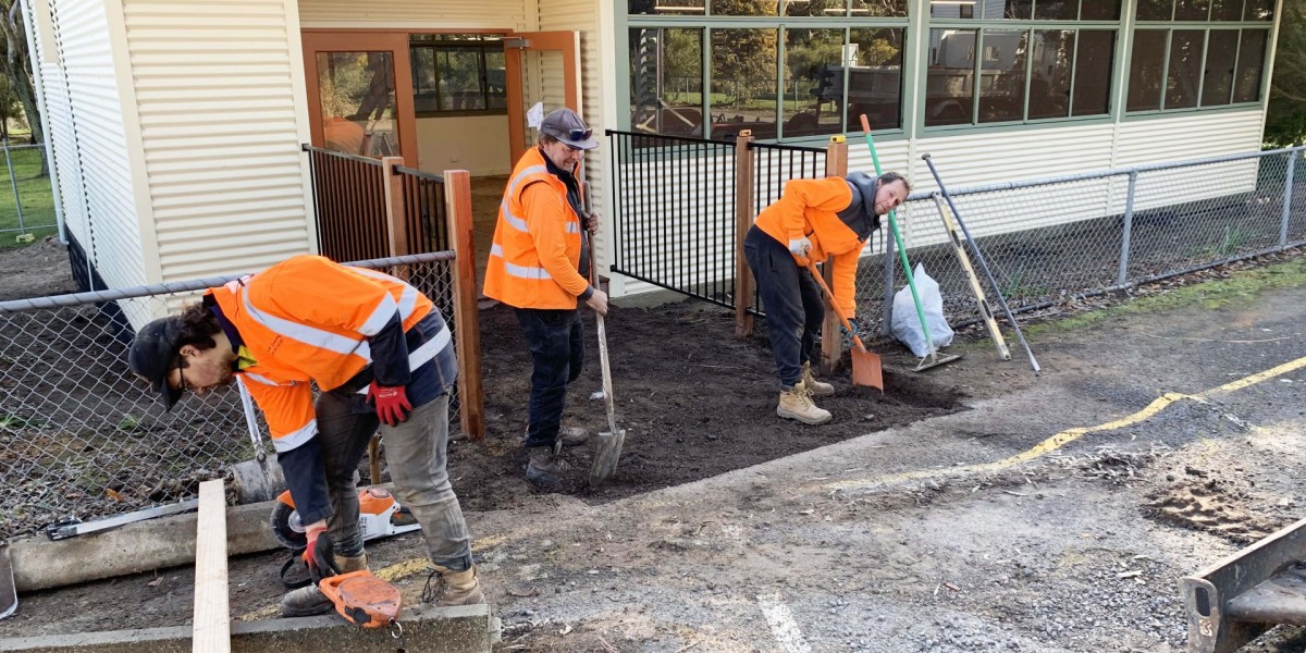 Three Workmen Digging in Front of Fenced Modular School Building