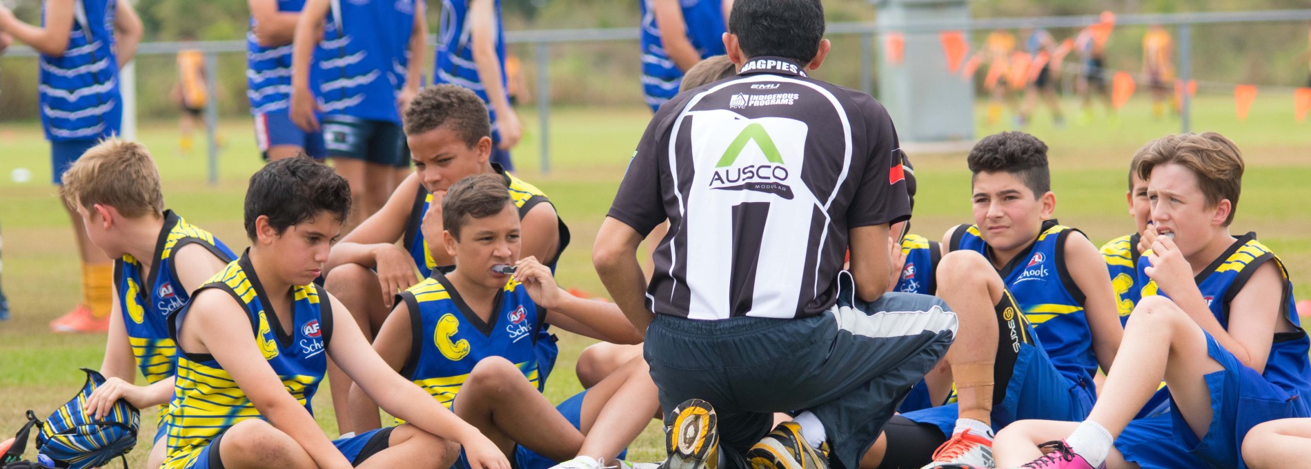 Young Male Sports Team Sitting on Field with a Coach