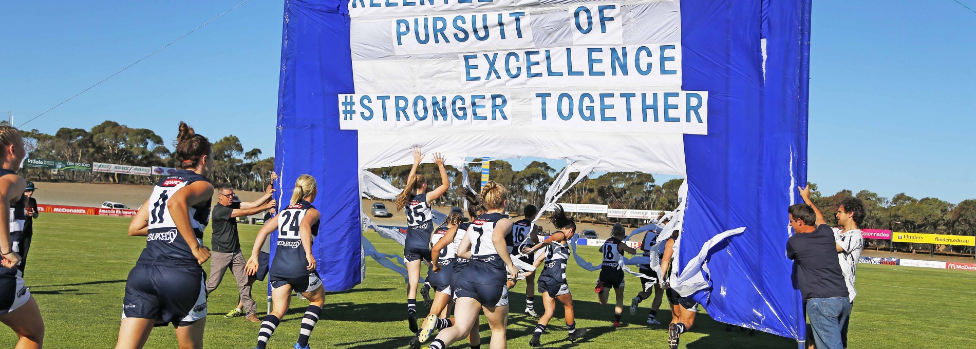 Women's Sports Team Running on Sports Field Beneath Flag