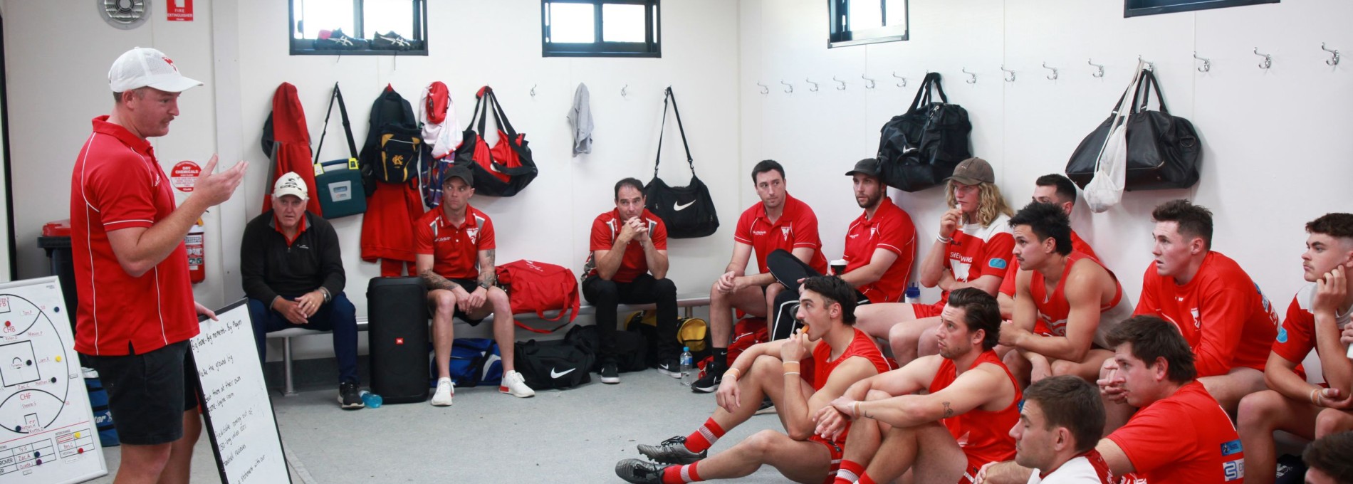 Male Sports Team Sitting in Changeroom with a Coach