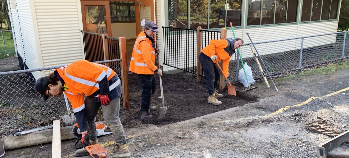 Three Workmen Digging in Front of Fenced Modular School Building