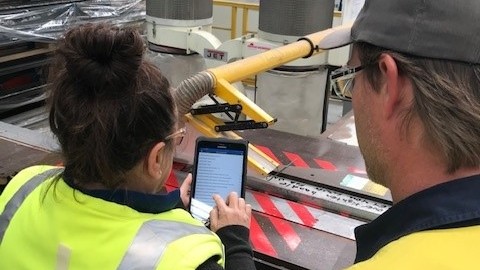 Woman and Man in High Vis looking at a Tablet with Factory Interior in Background